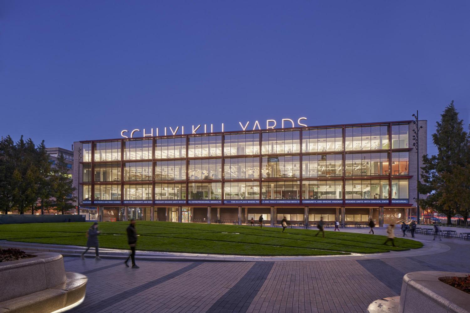 An image of the Schuykill Yards building at dusk, lit up from inside